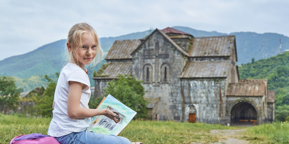 Blonde schoolgirl draws by chalk on the open air sitting on the ground