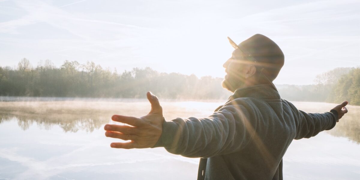 Young,Man,Arms,Outstretched,By,The,Lake,At,Sunrise,Enjoying