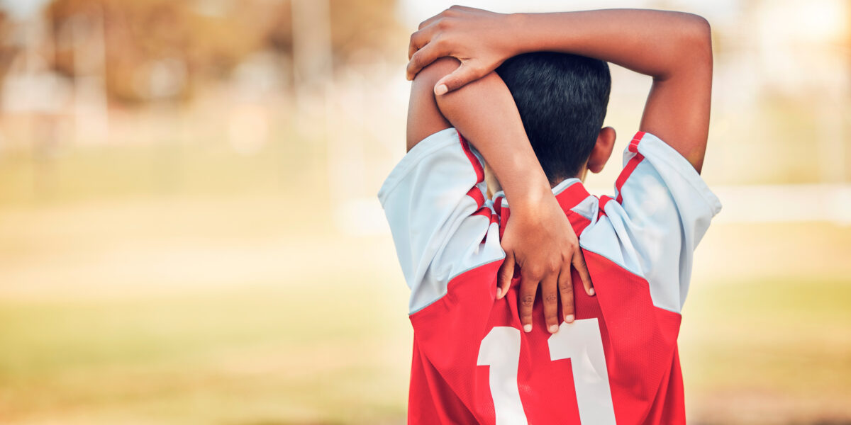 Soccer, football and boy stretching arm getting ready for training, game or competition. Sports, back view or soccer player warm up on grass field preparing for practice, exercise or workout outdoors