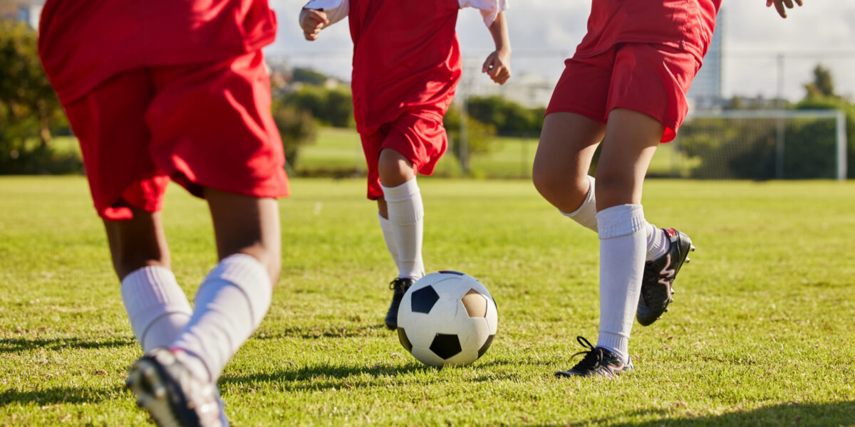 Kids team, soccer or legs with soccer ball in workout, fitness game or exercise on nature park grass, high school stadium or field. Football or sports training with energy in health or girls wellness